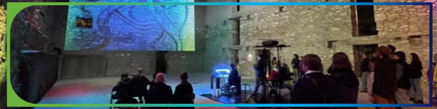 People seated in a stone courtyard at night watch a colorful abstract projection on a wall, with a 'Participate! City of Guelph' logo in the corner.