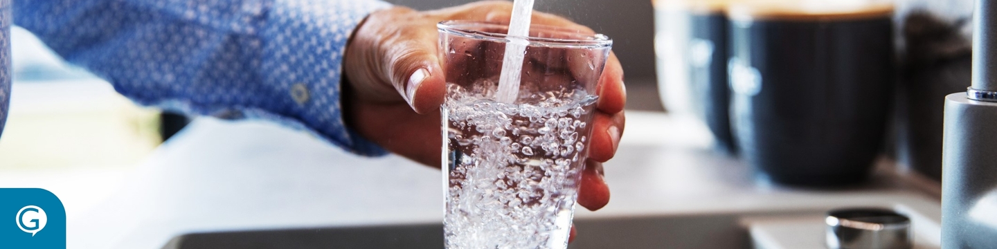 Person filling glass cup with water from the tap