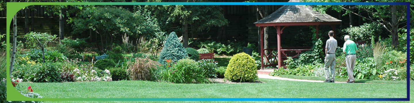 A vibrant garden with lush green grass, colorful flowers, and dense foliage. A red gazebo stands on the right side, with two people standing nearby, facing away from the camera.