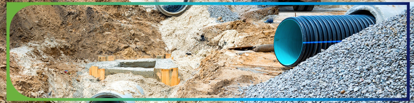 onstruction site with large pipes being installed underground. The ground is excavated, revealing dirt and gravel. There are several large concrete pipes and a blue corrugated plastic pipe visible in the scene.