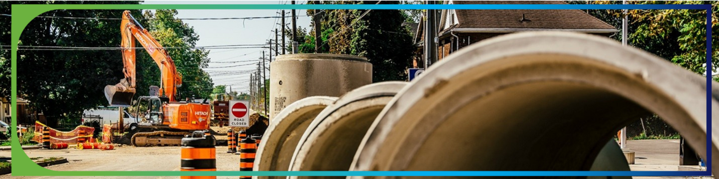View of road under construction with excavator in the background and big cement pipes in the front