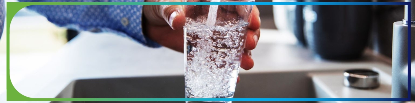 Person holding glass under kitchen tap to fill glass with water.