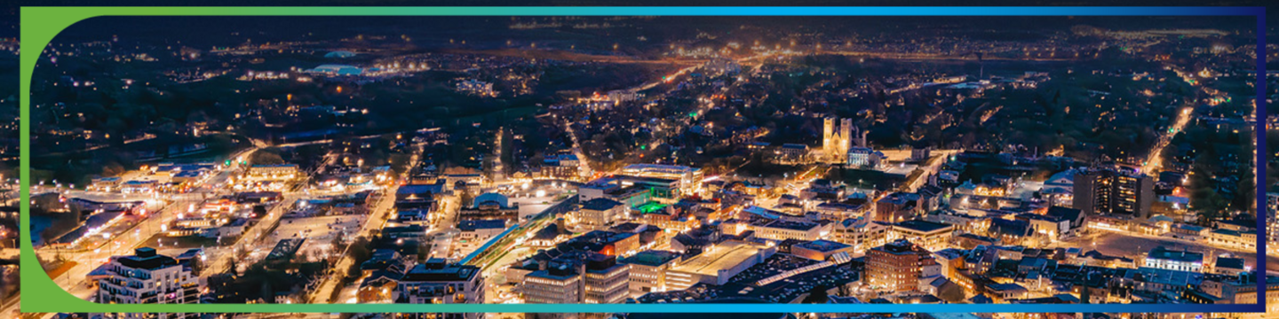 Aerial view of a city at night with numerous illuminated buildings and vibrant streetlights, showcasing a lively urban landscape under a dark sky.