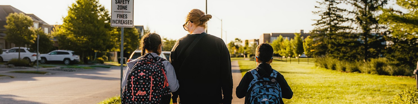 A parent with two children walk on a sidewalk next to a sign that reads "community safety zone - fines increased'