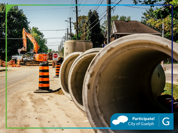 View of road under construction with excavator in the background and big cement pipes in the front. In the bottom right corner is a banner that reads "Participate! City of Guelph". 